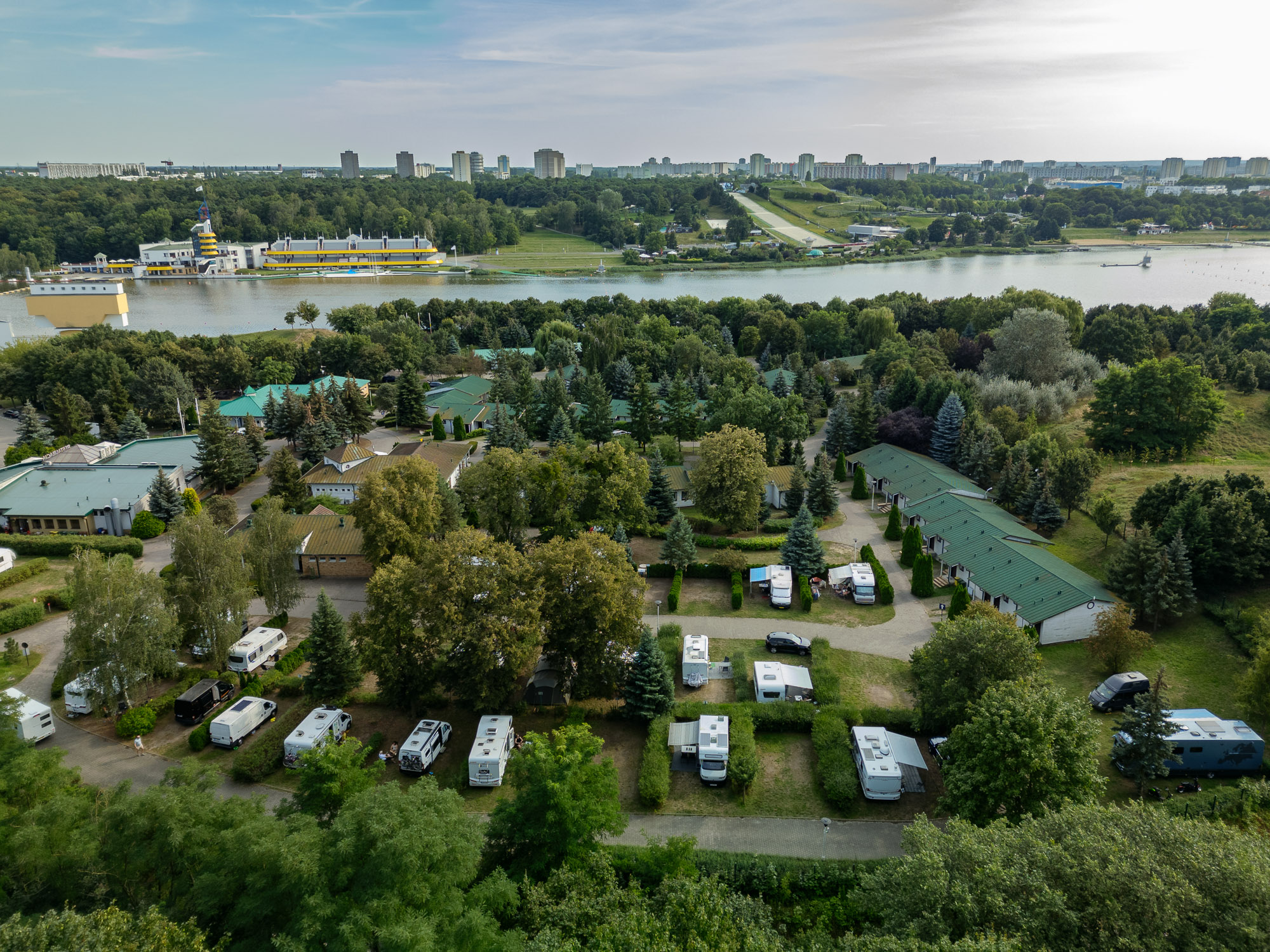 camping malta z lotu ptaka, na pierwszym planie pole campingowe, domki, zieleń. W drugim widoczne jezioro maltańskie i wieżowce